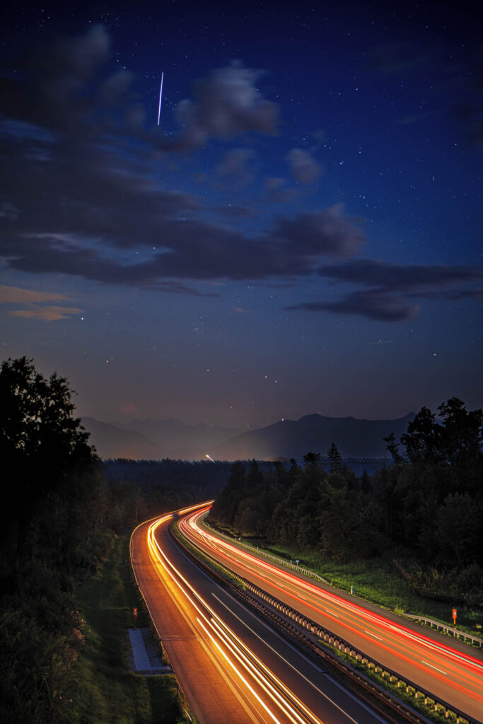 Leuchtspuren auf der Autobahn und Sternenhimmel mit Bergkette im Hintergrund - Start in der Astro-Fotografie