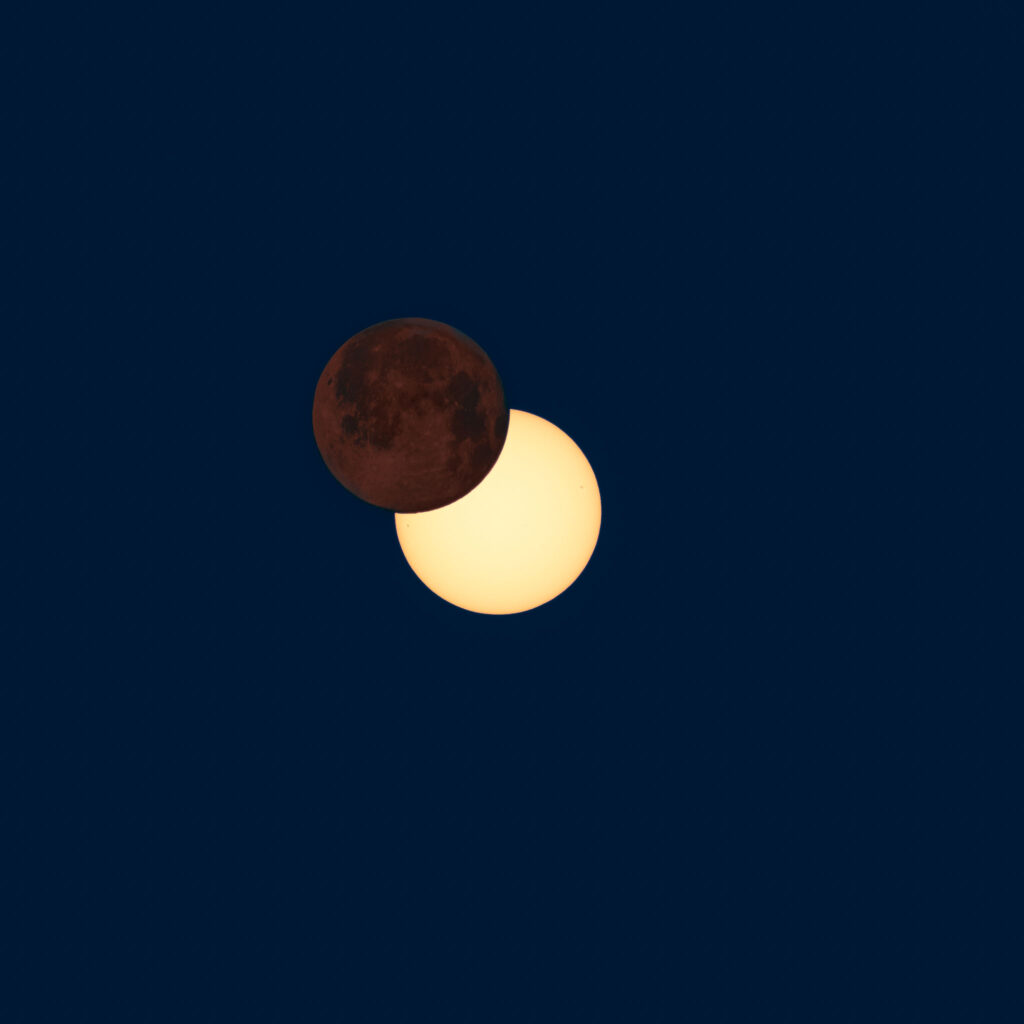Komposition eines rötlichen Neumondes und einer teilweisen Sonnenfinsternis